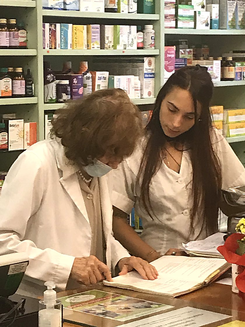 Bruna e Francesca al banco di Erba Amica consultano insieme un libro di riferimento