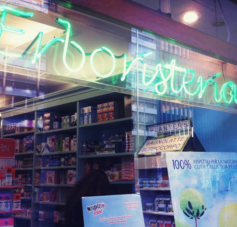L’insegna al neon con la scritta Erboristeria, vista dalla vetrina di Corso del Popolo